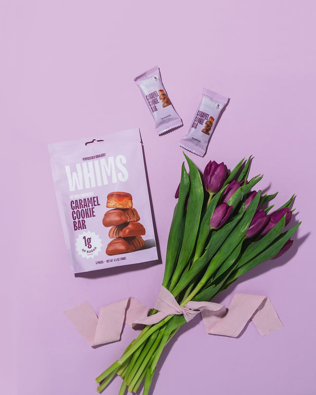 WHIMS Caramel Cookie Bar bag and individually wrapped pieces arranged with purple tulips on a lavender background